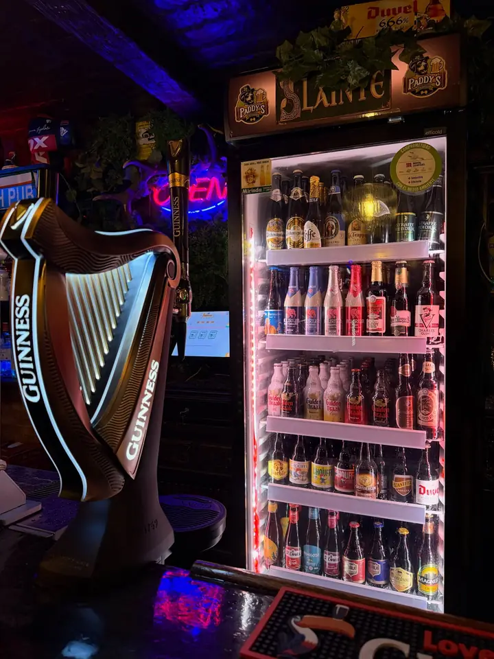 El arpa luminosa de Guinness junto a la nevera llena de botellas.