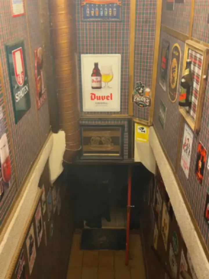 La escalera estrecha que baja al bar, con un cartel de Duvel al fondo