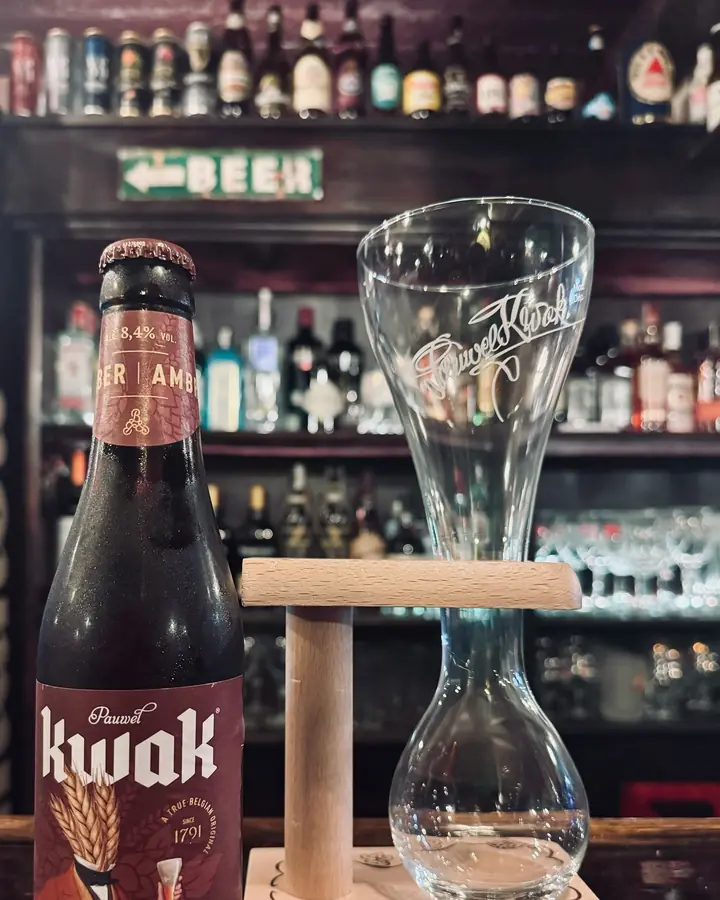 Botella de Kwak junto a su vaso de cochero en el soporte de madera.