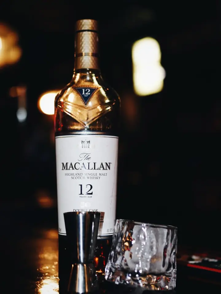 Botella de Macallan 12 con un vaso de whisky en la barra oscura.