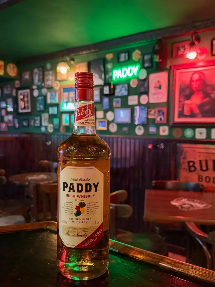 Una botella de Paddy Irish Whiskey con la pared verde del bar detrás.