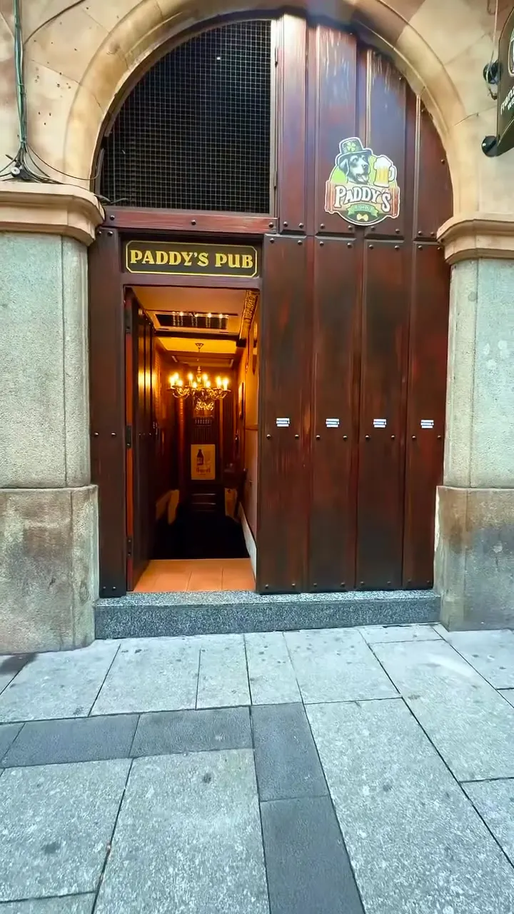 El portón de madera de Paddy’s en la Gran Vía, bajo un arco de piedra, con el pasillo iluminado al fondo