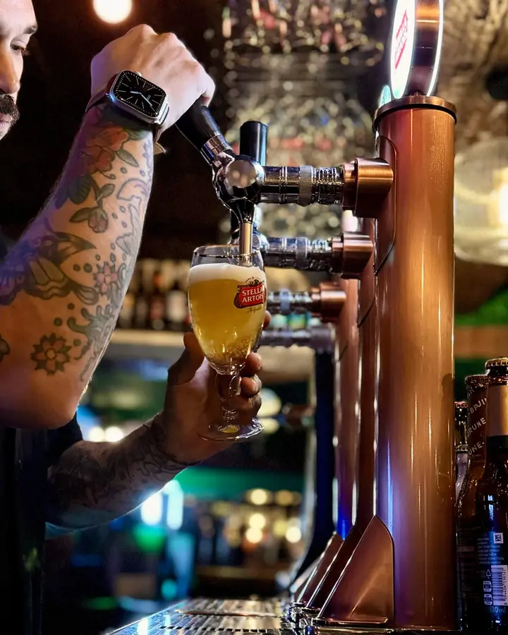 Un camarero tatuado tirando una Stella Artois del grifo.