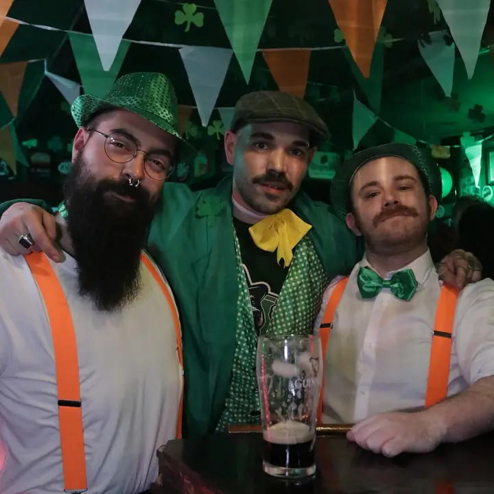 Tres clientes con tirantes y gorro verde en la barra el día de San Patricio.